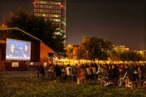 Skupina ľudí, ktorí v noci v Bratislave sledujú film v parku Jazero Kuchajda.