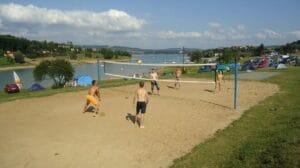 Partia ľudí hrajúcich volejbal na piesočnatej pláži pri jazere Domaša.