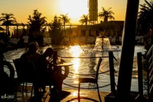 Dvaja ľudia sedia pri stole pri bazéne pri západe slnka na Letnom kúpalisku Plaza Beach Prešov.