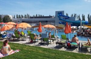 Návštevníci si užívajú Aquapark Trnava, posedenie pri bazéne s farebnými slnečníkmi.