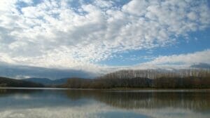 Vodná nádrž Suchá nad Parnou, jazero obklopené stromami a oblakmi.