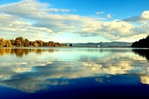 Vodná nádrž Kanianka, malebné jazero so stromami a oblakmi odrážajúcimi sa v jeho pokojných vodách.